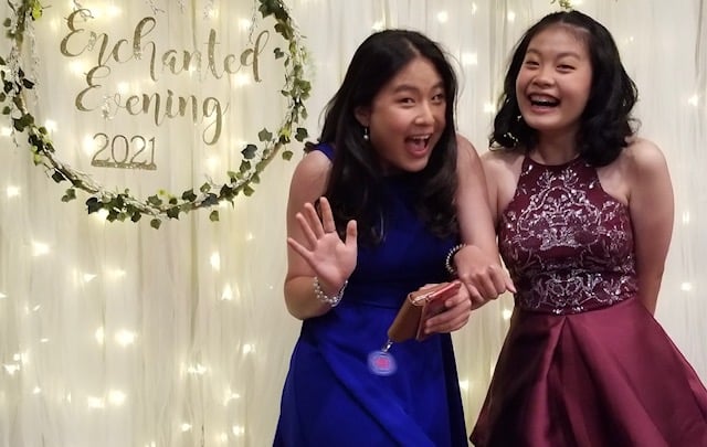 two asian teenage girls dressed for school dance smiling and laughing together