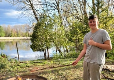 Teenage boy roasting a hotdog over a fire