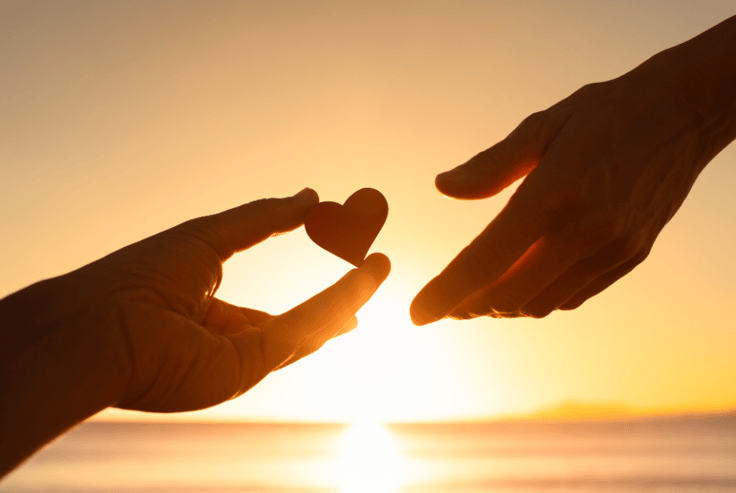 two hands with heart figure and sunset behind