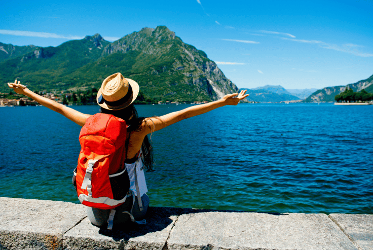 girl sitting on wall beside lake