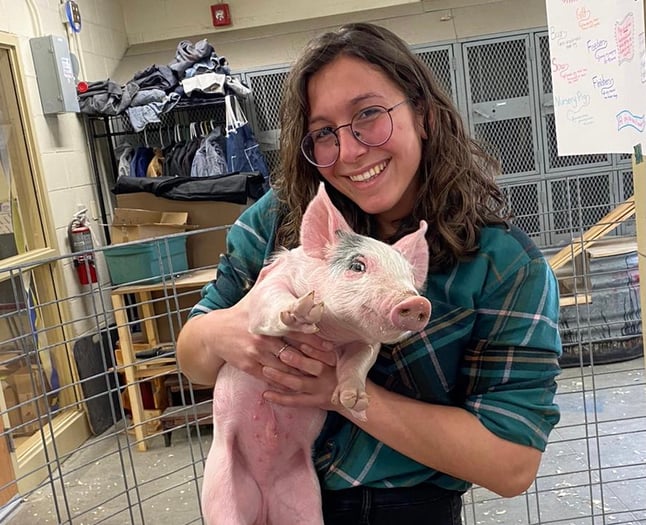 Vanessa smiling and holding a piglet