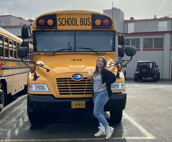 girl posing in front of school bus with coffee in hand