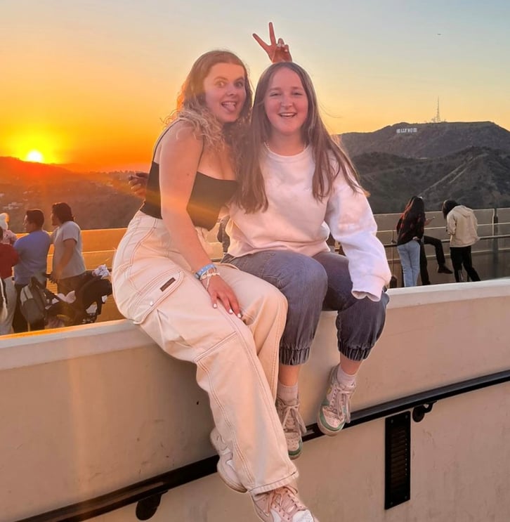 two girls sitting on wall with sunset behind