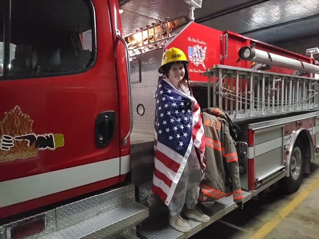 girl wrapped in American flag standing on fire truck
