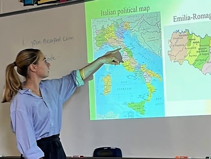 Anna in classroom pointing to map of Italy