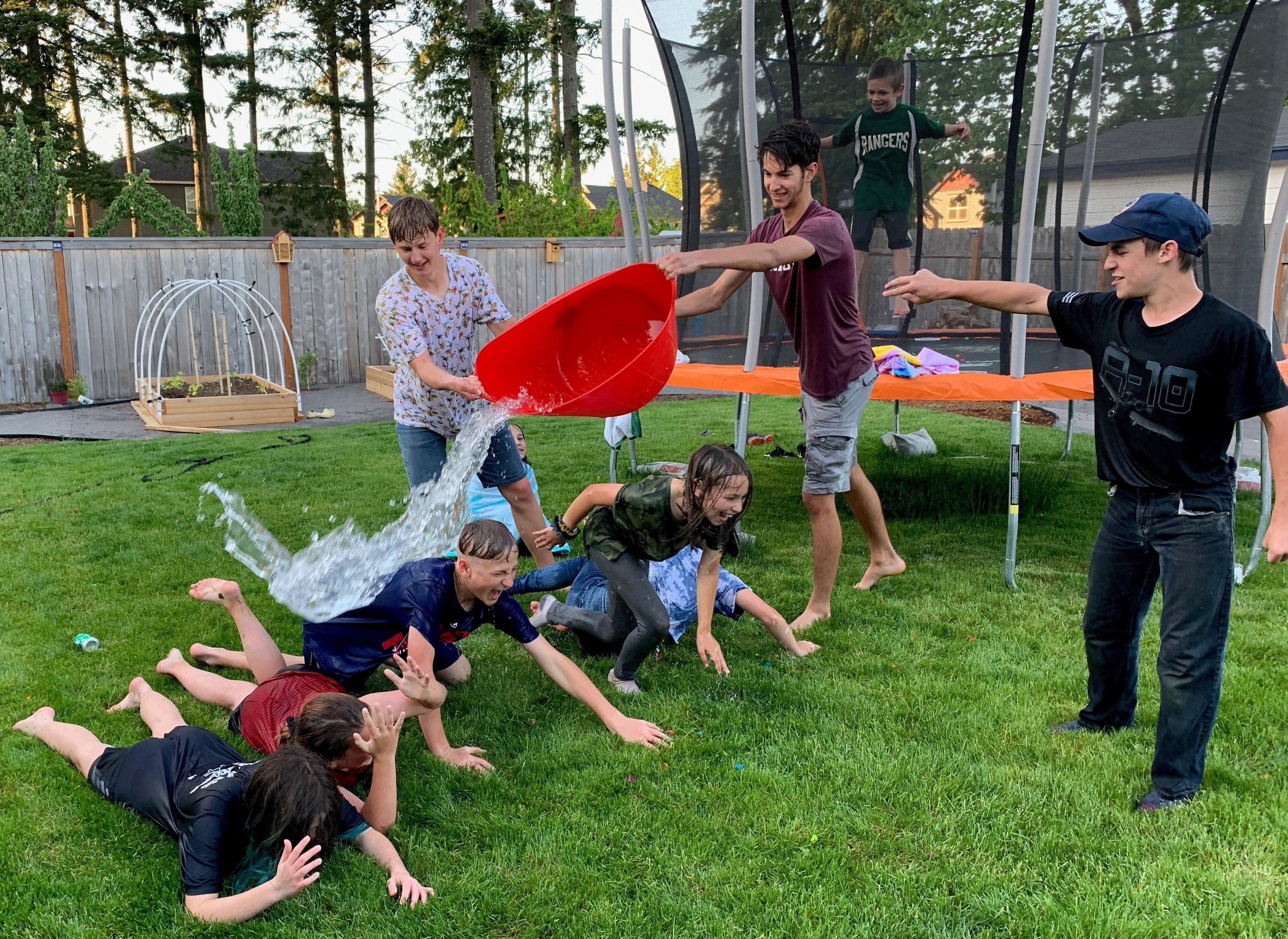 teenage boy dumps bucket of water and laughing children in back yard