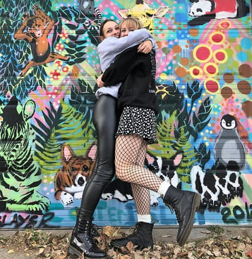 two teen girls hugging in front of a colorful mural