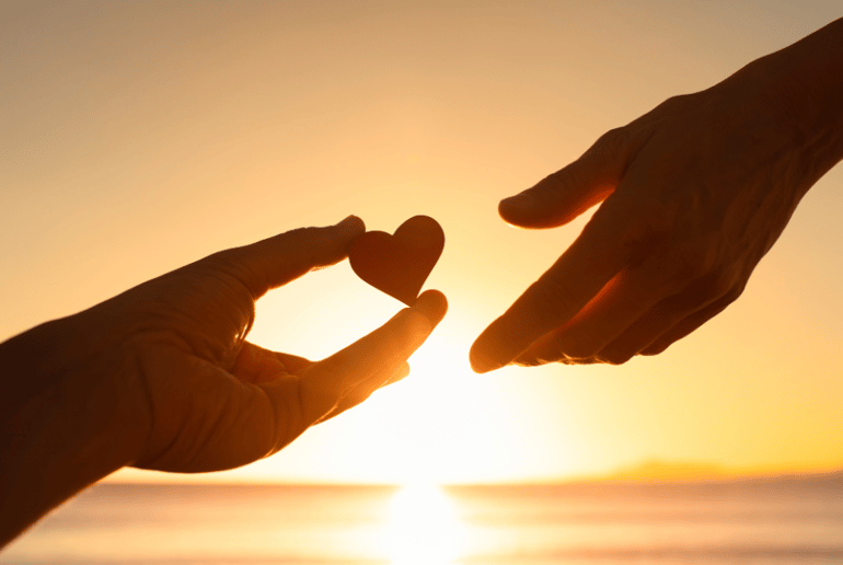 sunset behind two hands sharing a heart