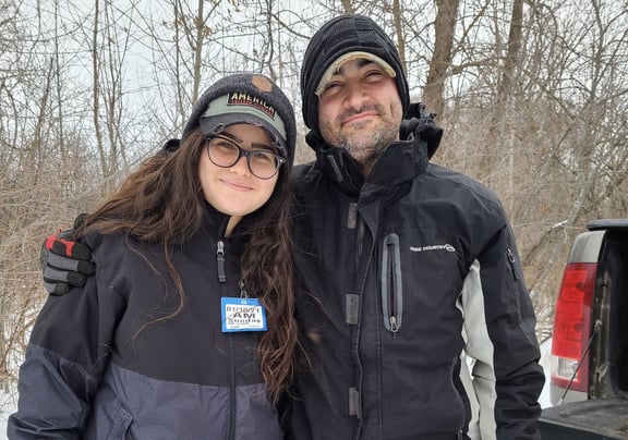 Father and daughter standing in the snow with trees in background