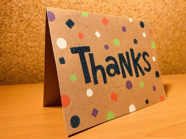 a thank you card on a desk in front of a bulletin board