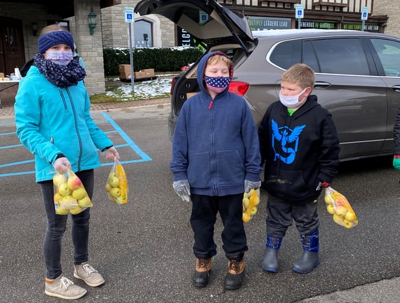 Jana and host brothers holding bags of apples outside.