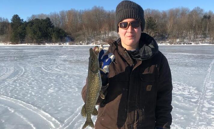 Teenage boy standing on ice holding a fish