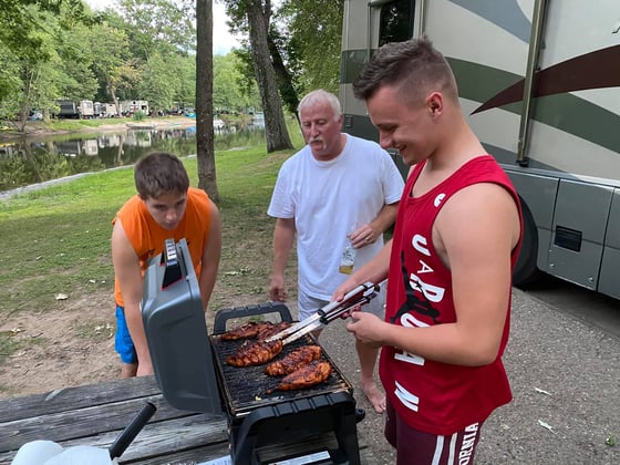 teen boy bbq'ing chicken with dad and brother