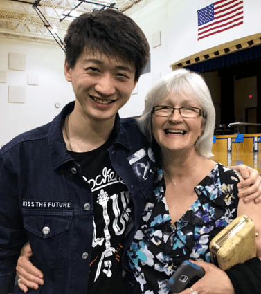 Asian boy with arm around smiling older teacher