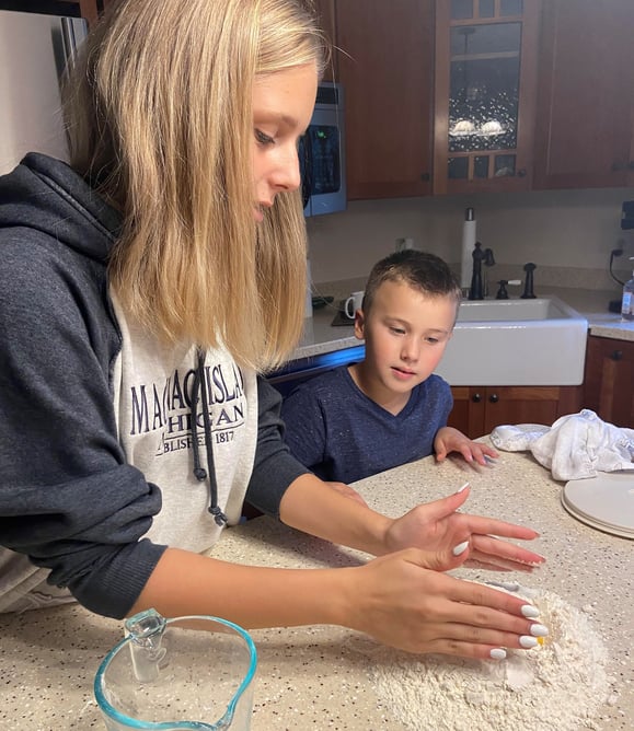 teen girl making dough with young boy looking on