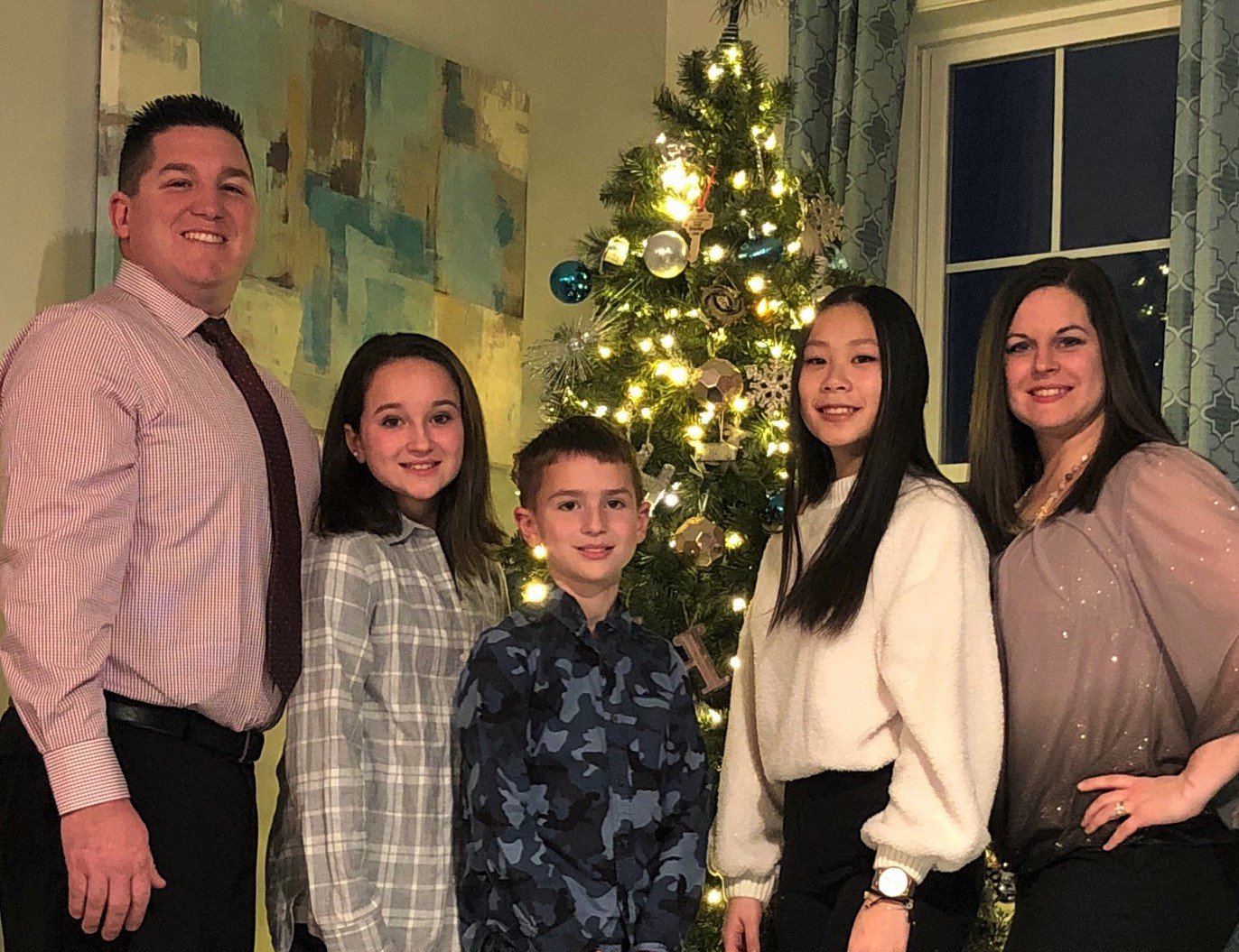 Mother, father, son and daughter with spanish exchange student in front of Christmas tree