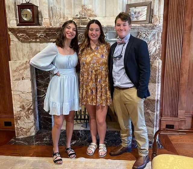 three teens in dress clothes in front of the mantle