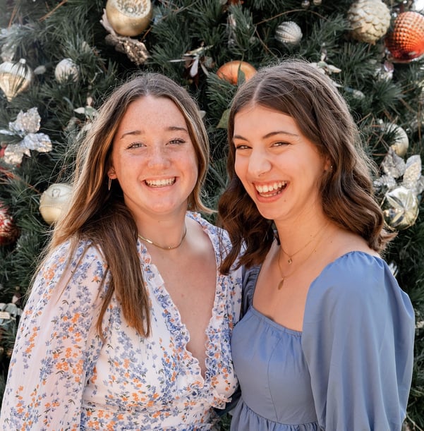 two teen girls smiling in front of a Christmas tree