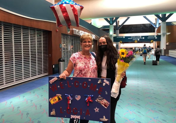 woman and exchange student at airport with sign and balloons