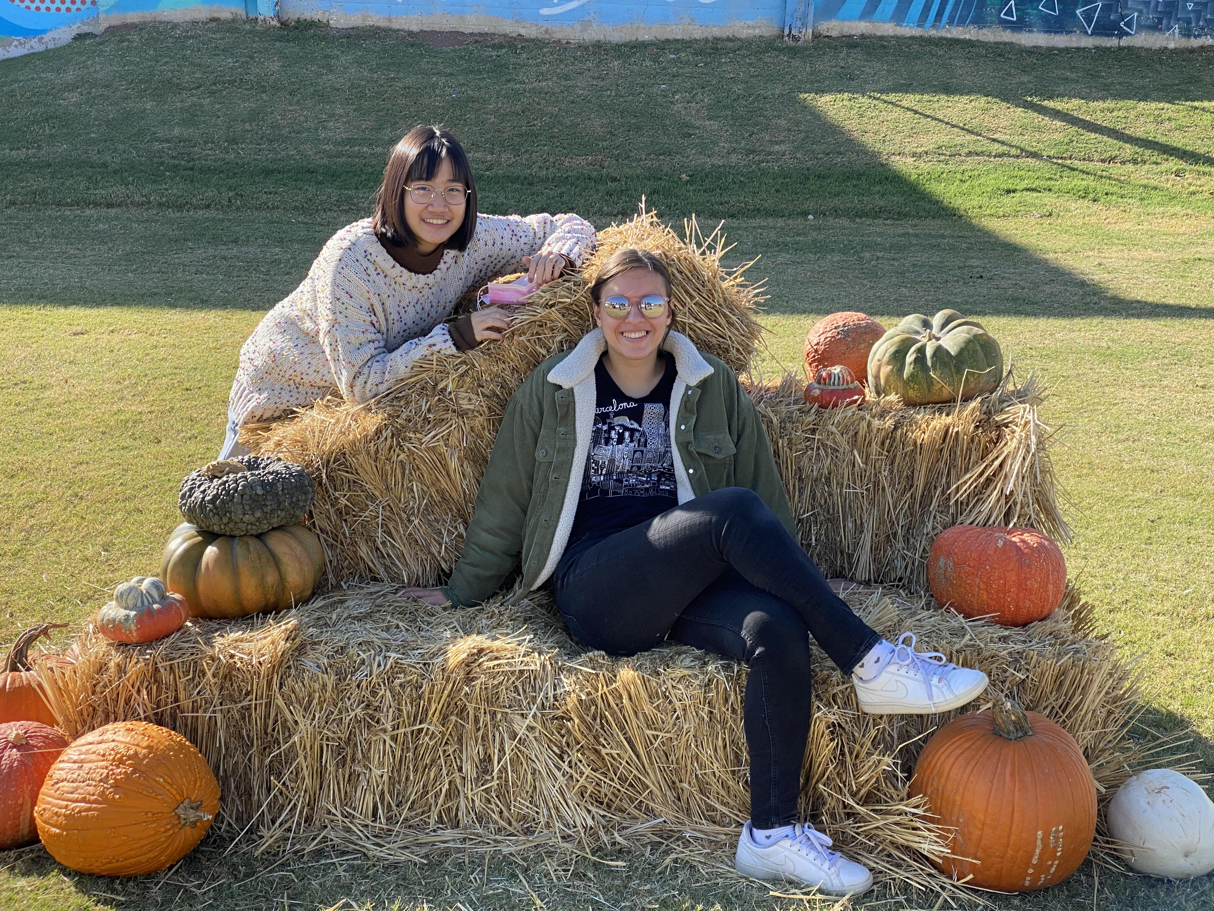 two teen girls sitting on hay bales surrounded by pumkins