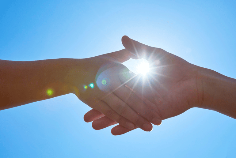 Two people's hands holding each other in front of a ray of sun