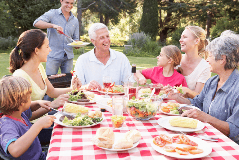 Photo of a family with kids eating a meal together outside and laughing