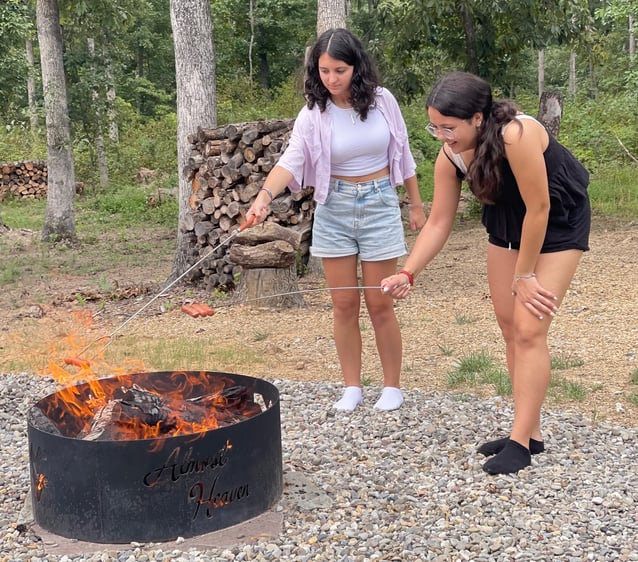 two girls roasing hot dogs over campfire