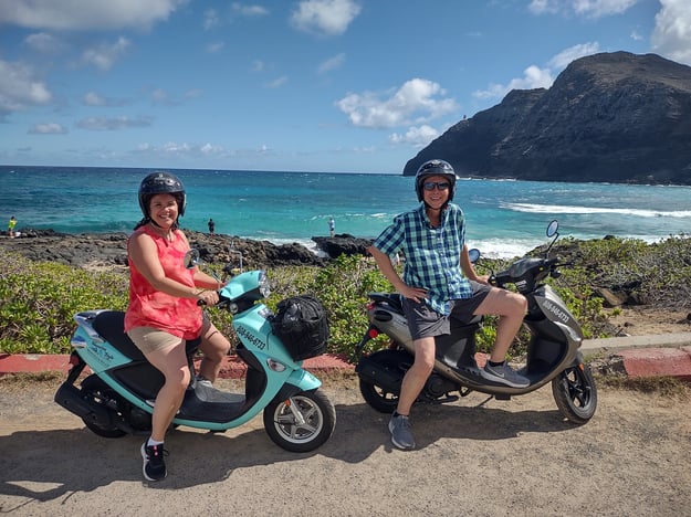 couple on scooters in front of ocean