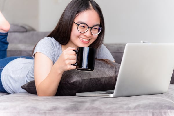 smiling Asian girl on laptop and holding a mug