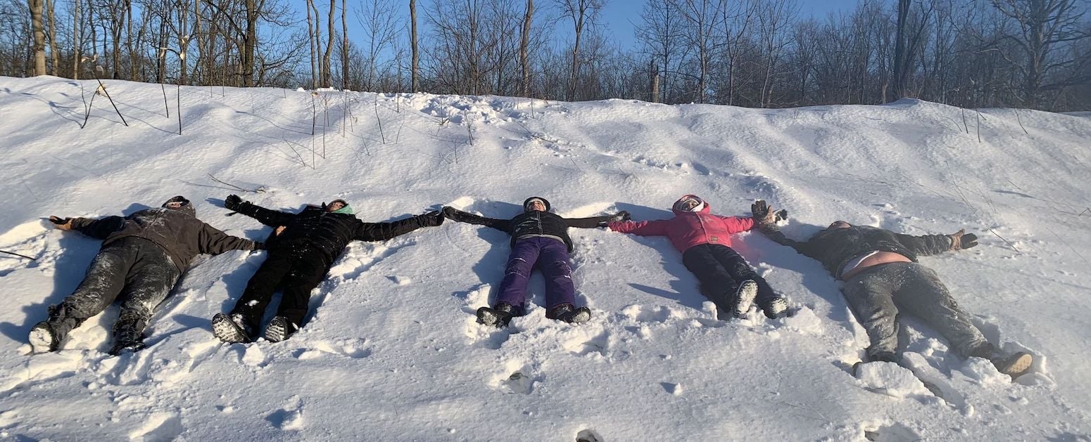 Student from Thailand laying in the snow with host family