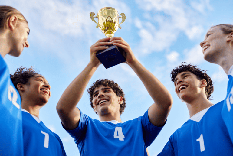 Teenage boy holding up trophy with his sports teammates