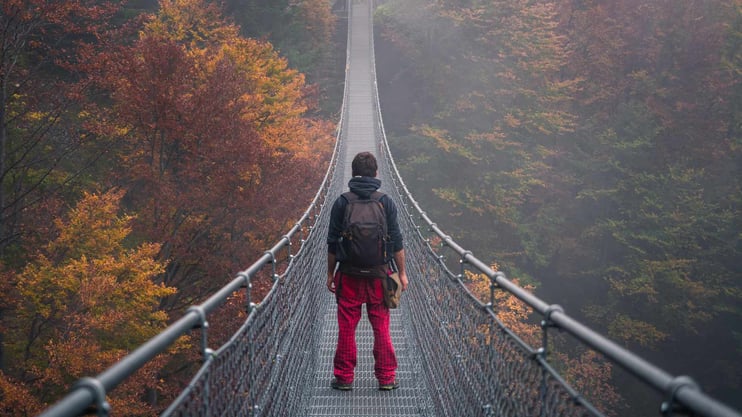 Teenage boy standing on a suspension bridge looking across