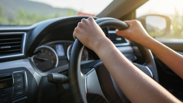 Two hands on a steering wheel driving a car