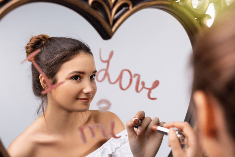 Teenage girl writing "I love me" on a mirror with her reflection