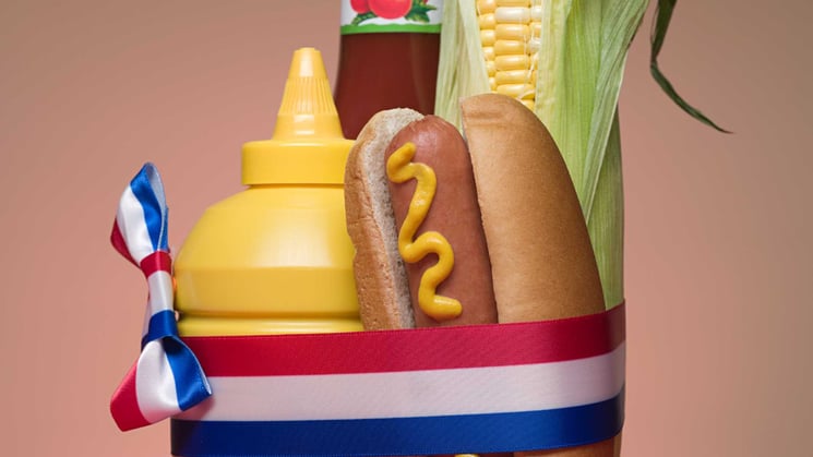 a hot dog with ketchup mustard and corn wrapped in red white and blue ribbon