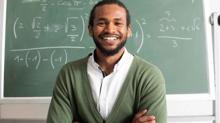 a smiling teacher in front of blackboard with math problems