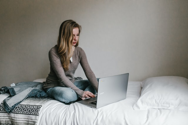 a teenage girl in her room on her bed working on her computer
