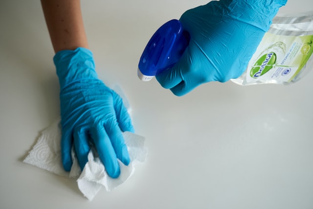 two hands wearing blue rubber gloves and cleaning a counter
