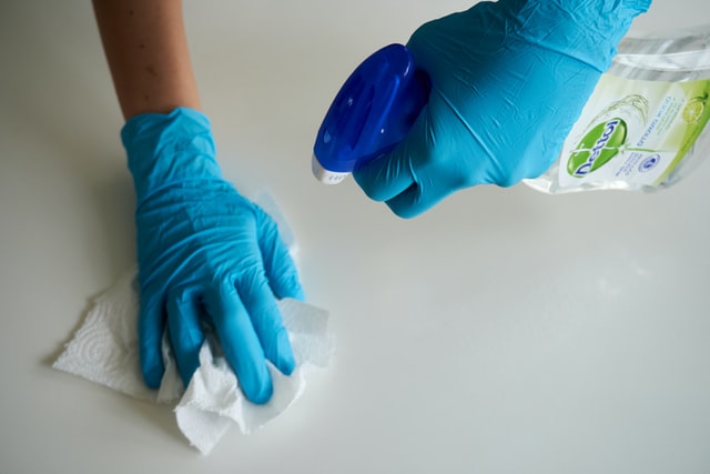 hands wearing blue rubber gloves cleaning counter with spray bottle