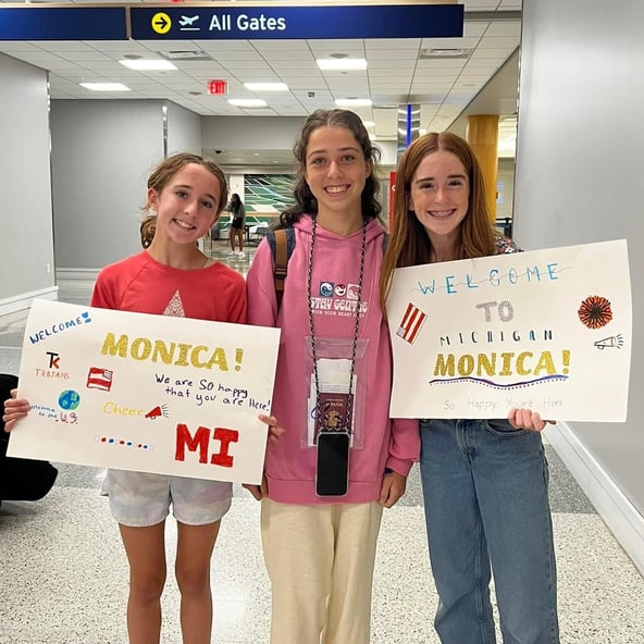 3 girls at airport with welcome signs