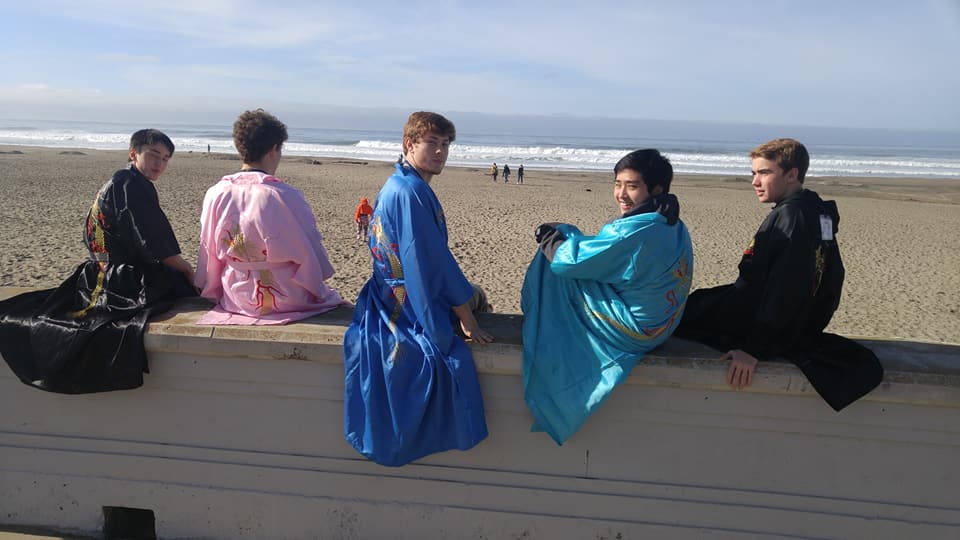 five teen boys sitting on wall at beach