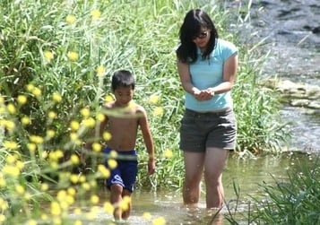 big sister and little brother wading in stream together