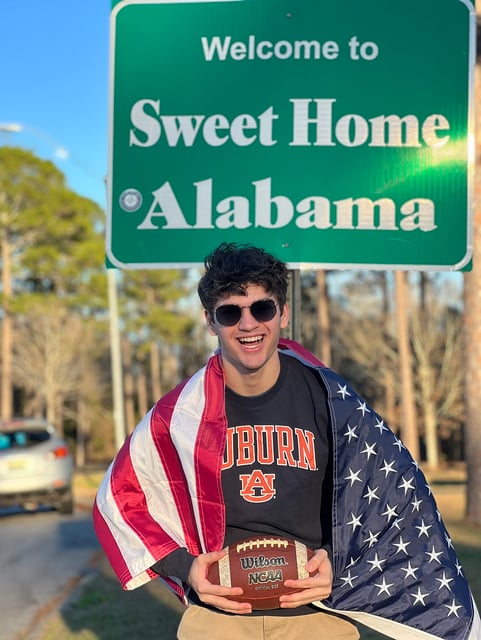 boy with American flag holding football in front of Alabama sign