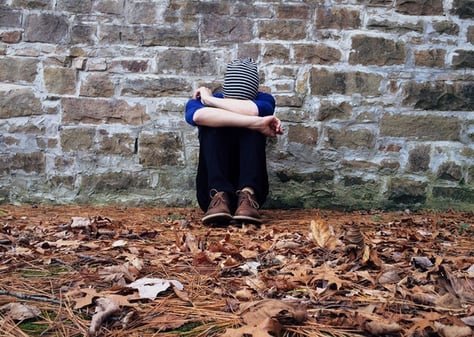 boy sitting against a wall with head in hands to illustrate culture shock symptoms and emotions