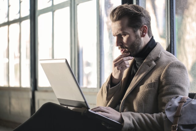 father sitting with laptop looking at screen with worried expression