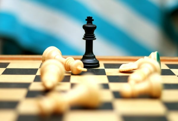 black chess king piece standing among knocked over white pieces