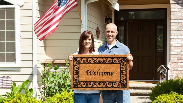 couple holding welcome mat with US flag in the background