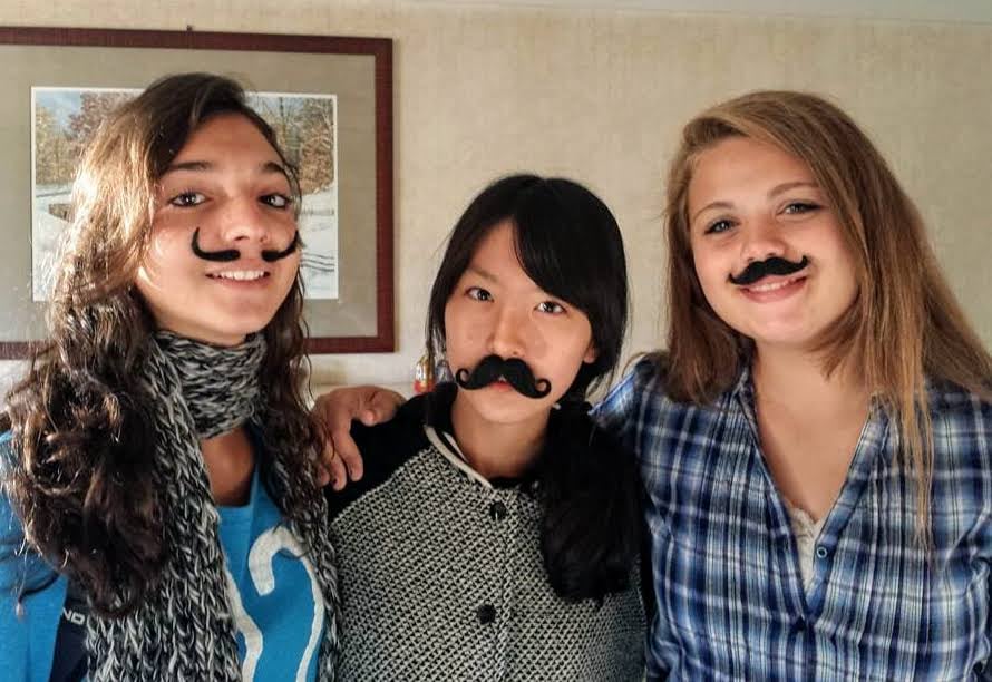 three smiling teenage girls with fun, fake moustaches