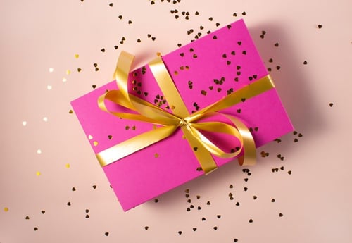 a package wrapped in pink paper with gold ribbon and glitter