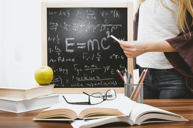 student pointing chalk to blackboard showing E=mc2 and math formulas